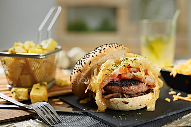 Köstliche Gourmet-Burger mit Patty, Zwiebeln und Käse serviert mit Kartoffelkeilen — Stockfoto