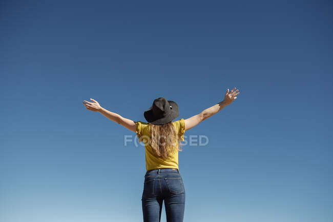 De baixo mulher de pé com as mãos afastadas contra o céu azul sem nuvens — Fotografia de Stock