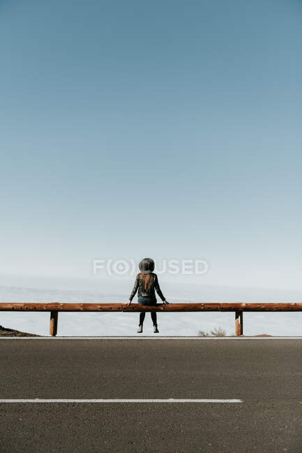 Visão traseira da mulher turística sentada na cerca de madeira na borda da colina — Fotografia de Stock