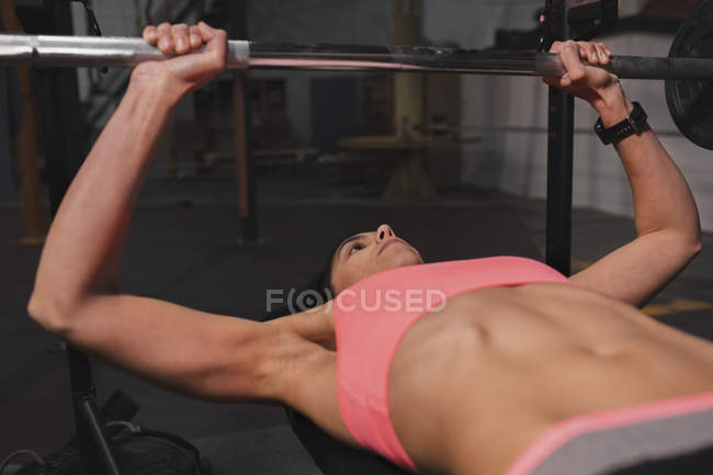 Frau in Sportkleidung macht Übungen mit Langhanteln auf Bankdrücken im Fitnessstudio — Stockfoto