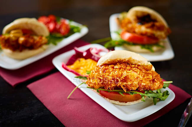 Hambúrgueres apetitosos com tomates e frango crocante em placas escuras em gastrobar — Fotografia de Stock