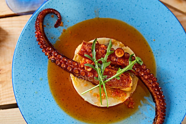 Grilled octopus served with sauce on polenta on blue plate on wooden table — Stock Photo