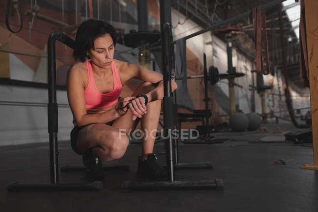 Frau in Sportbekleidung überprüft Uhrzeit und sitzt im Fitnessstudio zwischen parallelen Stangen — Stockfoto