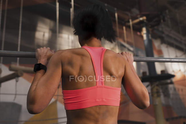 Visão traseira da mulher em sportswear fazendo puxar para cima exercícios na barra horizontal no ginásio — Fotografia de Stock