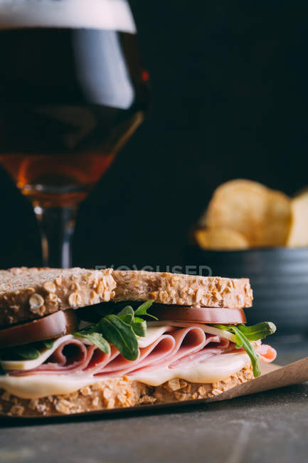 Leckeres Sandwich mit Schinken, Käse und Gemüse mit einem Glas Bier und Pommes auf dunklem Hintergrund — Stockfoto