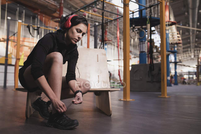 Side view of woman in sportswear with headphones listening music and lacing shoe in gym — Stock Photo