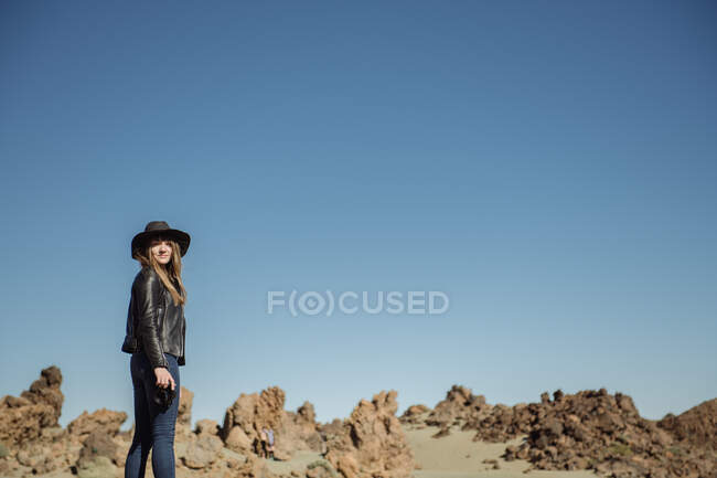 Fotógrafa feminina em pé com câmera e olhando para colinas no deserto — Fotografia de Stock