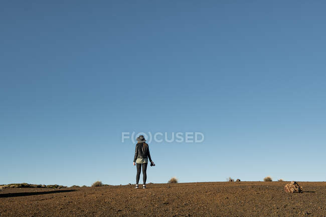 Вид ззаду на жінку-фотографа, що стоїть з камерою і дивиться на пагорби в пустелі — стокове фото