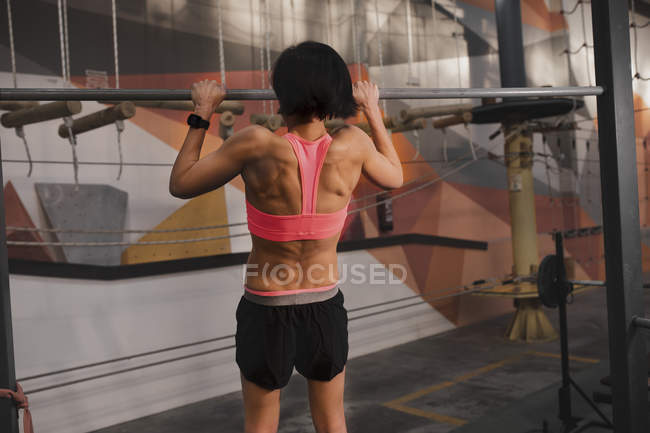 Back view of woman in sportswear doing pull up exercises on horizontal bar in gym — Stock Photo