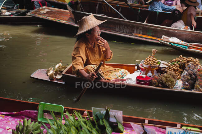 Ásia sênior adulto mulher fumar cigarro e vela no barco com bens — Fotografia de Stock