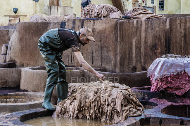 31 December 2017 - Marrakesh, Morocco: Side view of adult man preparing animal skin for making leather on outdoors factory — Stock Photo