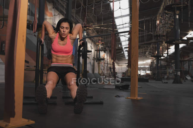 Frau in Sportbekleidung macht in großer Turnhalle Klimmzugübungen am parallelen Barren — Stockfoto