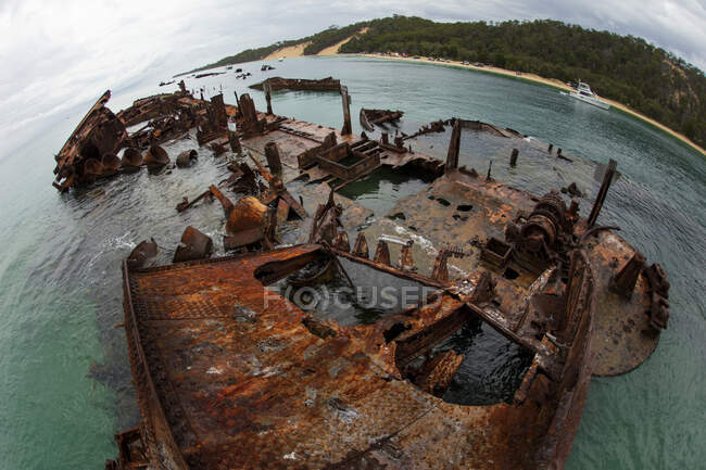 Над широким углом ржавый корабль разбился на зеленом берегу в голубой океанской воде. — стоковое фото