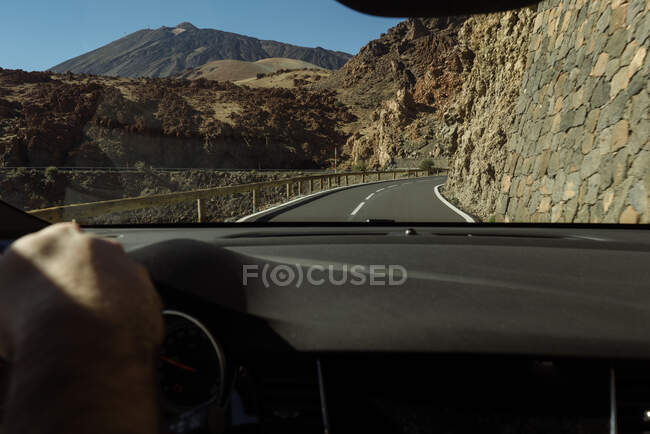 Crop hand of driver holding steering wheel and moving to mountains on rural road — Stock Photo