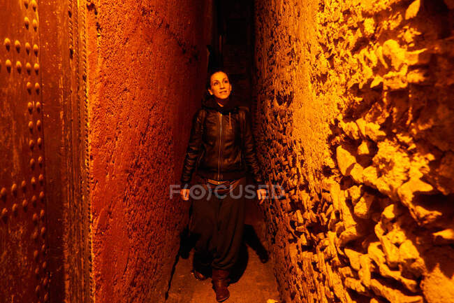 31 December 2017 - Marrakesh, Morocco: Woman in dark clothes walking on narrow street at rough wall in the evening — Stock Photo