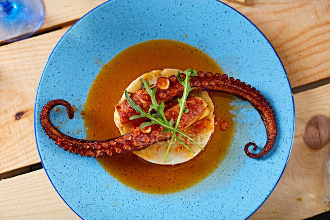 Gegrillter Oktopus mit Soße auf Polenta auf blauem Teller auf Holztisch — Stockfoto