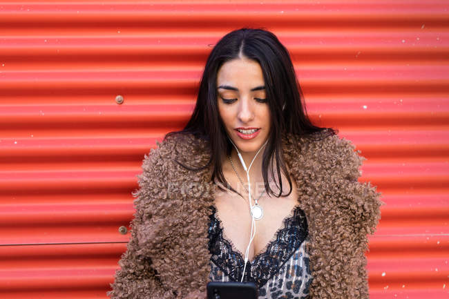 Trendy woman with smartphone near wall — Stock Photo