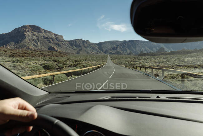 Crop hand of driver holding steering wheel and moving to mountains on rural road — Stock Photo