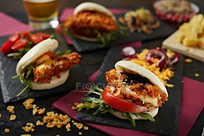 Appetizing burgers with tomatoes and crispy chicken on dark plates in gastrobar — Stock Photo