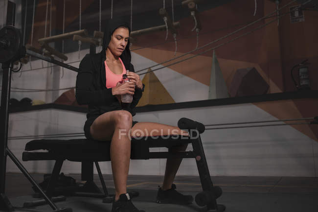 Mujer en ropa deportiva comprobar el tiempo de guardia y sentado en el banco en el gimnasio - foto de stock