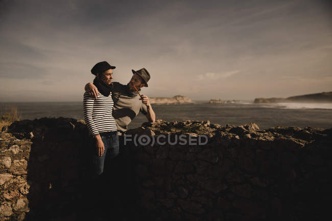 Vista lateral do elegante casal elegante perto de rochas na costa perto do mar e do céu maravilhoso — Fotografia de Stock