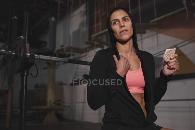Frau in Sportbekleidung mit Energie-Reiskuchen sitzt auf Bank im Fitnessstudio — Stockfoto