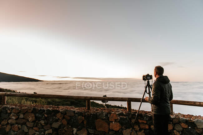 Боковой вид неузнаваемого мужчины-фотографа, стоящего с камерой и фотографирующего с холма — стоковое фото