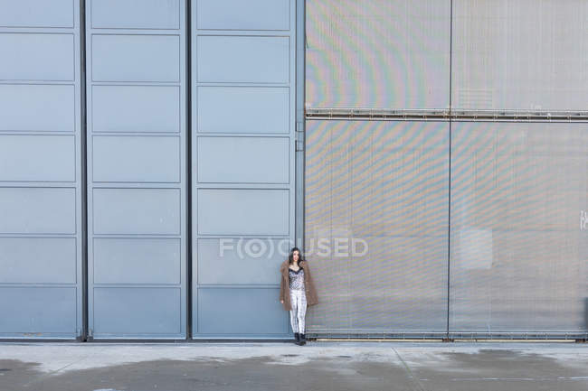 Woman in stylish outfit standing on sidewalk near walls of modern buildings on city street — Stock Photo