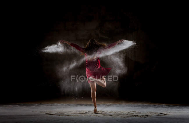 Young woman dancing and using powder in darkness — Stock Photo