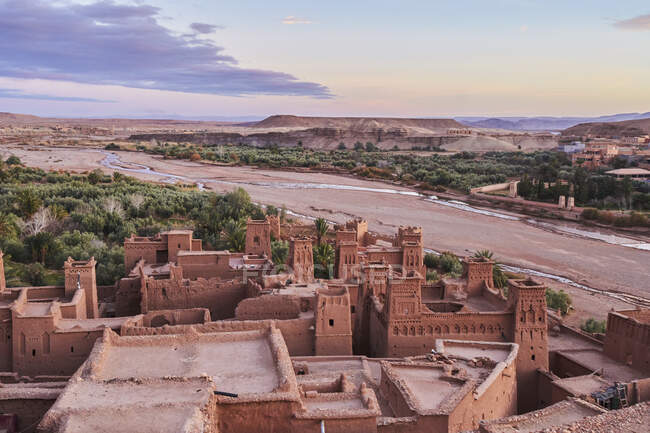 Da cidade velha acima com construções de pedra perto do rio estreito entre o deserto e o céu bonito com nuvens em Marraquexe, Marrocos — Fotografia de Stock
