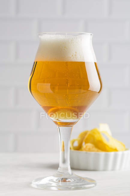 Glass of beer and potato chips on white background — Stock Photo