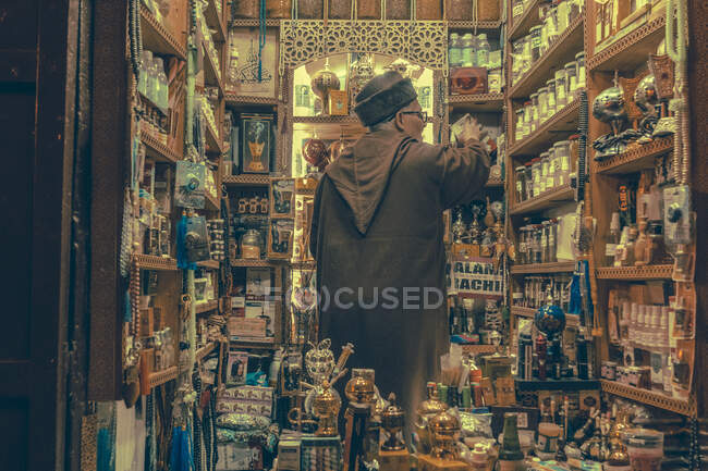 31 December 2017 - Marrakesh, Morocco: Back view of elder man taking box while working in souvenir shop in market — Stock Photo