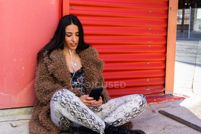 Trendy woman with smartphone near wall — Stock Photo
