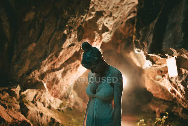 Чуттєва жінка в білій білизні і сухий порошок на тілі, що стоїть в освітленій скельній печері — стокове фото