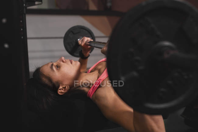 Mulher em sportswear fazendo exercícios com sinos no supino no ginásio — Fotografia de Stock
