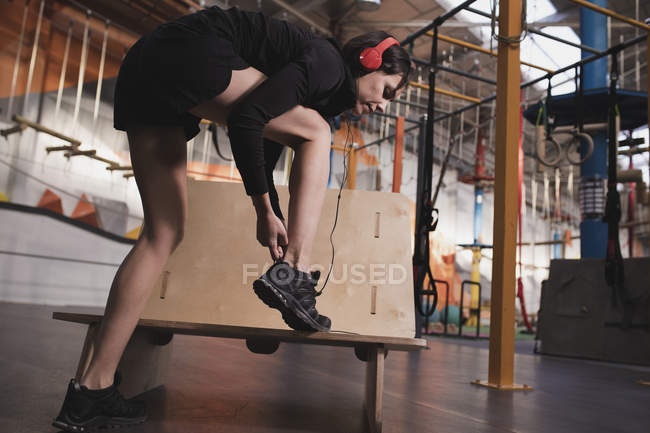 Side view of woman in sportswear with headphones listening music and lacing shoe in gym — Stock Photo