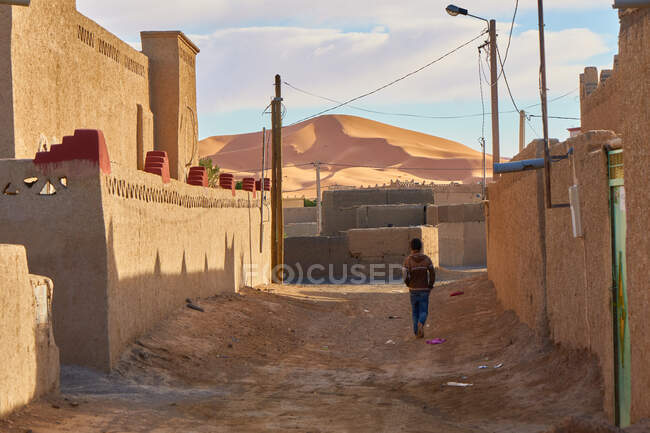 Vista posterior de humanos que van entre las construcciones de piedra de la ciudad vieja entre el desierto en Marrakech, Marruecos - foto de stock