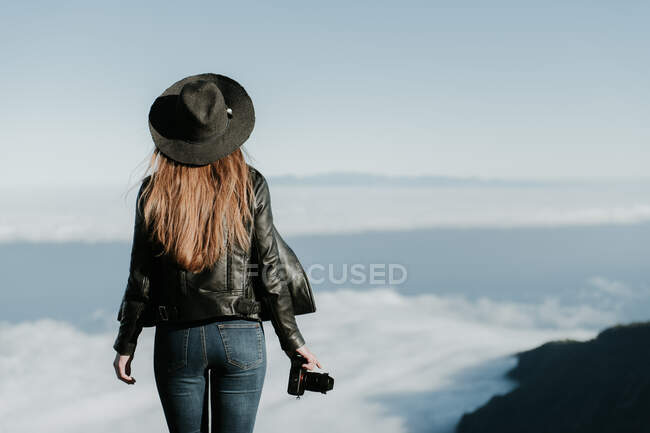 Rückansicht einer Frau mit Fotokamera, die oben auf dem Hügel steht und die Wolkenlandschaft betrachtet — Stockfoto