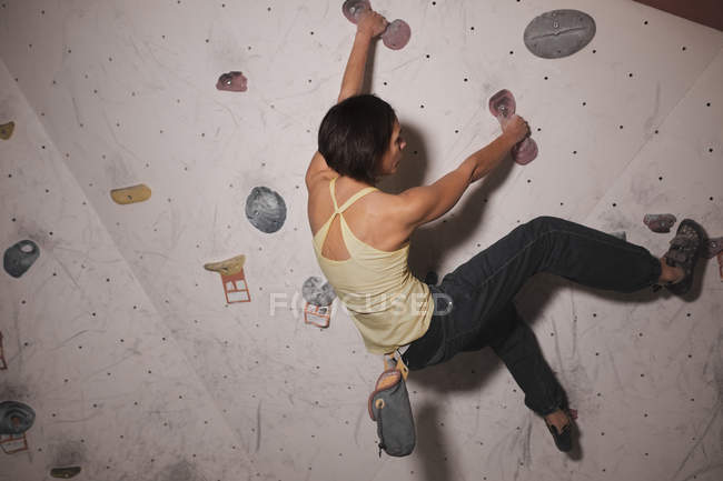 Back view of woman in sportswear training on climbing wall with holds in gym — Stock Photo