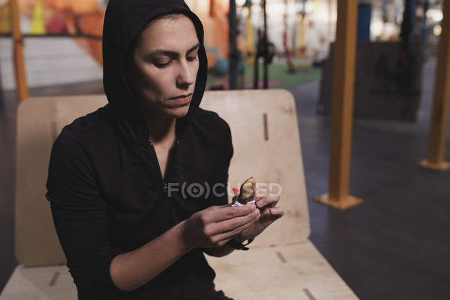 Frau in Sportbekleidung mit Energieriegel sitzt auf Bank im Fitnessstudio — Stockfoto