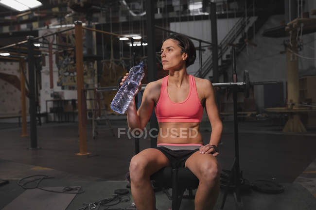 Mulher em sportswear com garrafa de água sentado no banco no ginásio — Fotografia de Stock