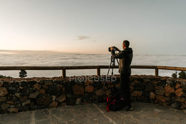 Side view of unrecognizable male photographer standing with camera and taking shots of view from hill — Stock Photo