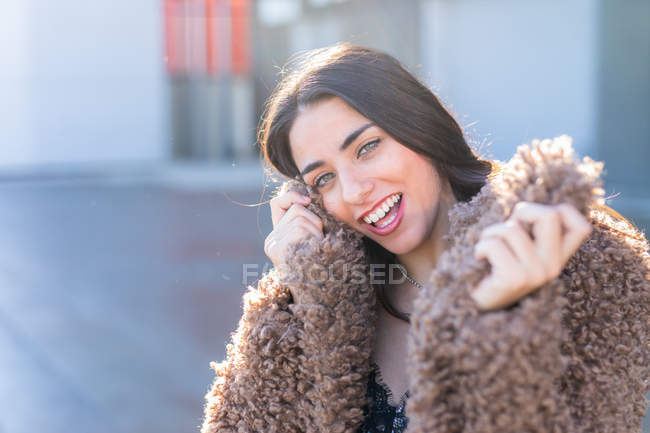 Cheerful woman wrapping in coat on street — Stock Photo