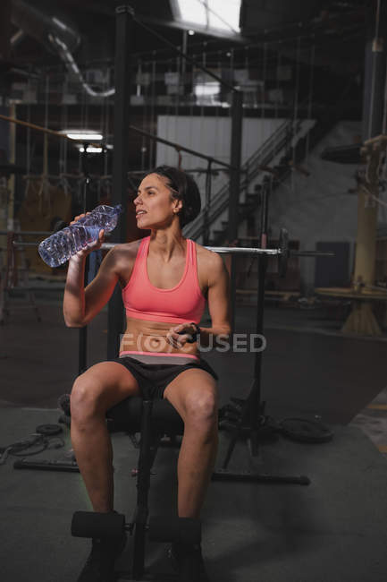Жінка в спортивному одязі з пляшкою води, що сидить на лавці в спортзалі — стокове фото