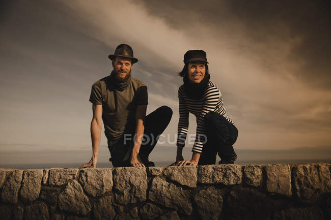 Stylish elegant couple leaning out from rocks and wonderful sky with clouds — Stock Photo