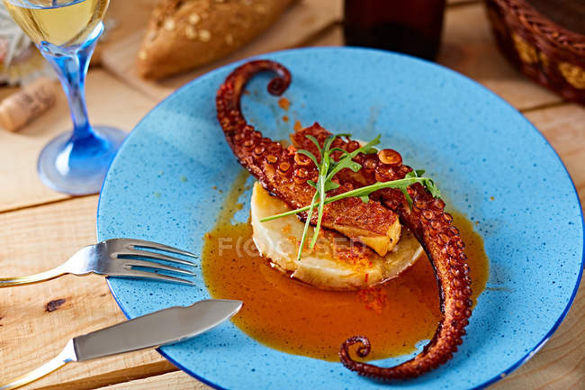 Polpo grigliato servito con salsa su polenta su piatto blu su tavolo di legno — Foto stock