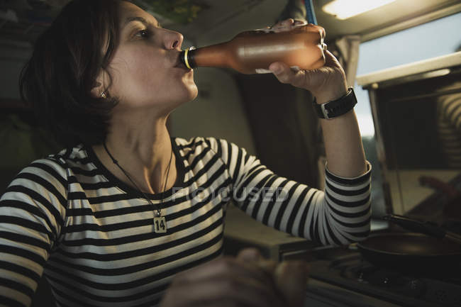 Jovem morena bebendo água de garrafa perto do fogão em casa móvel — Fotografia de Stock