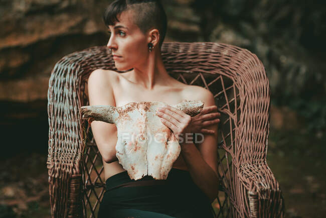 Donna in topless con il cranio bovino seduto su una sedia di vimini — Foto stock