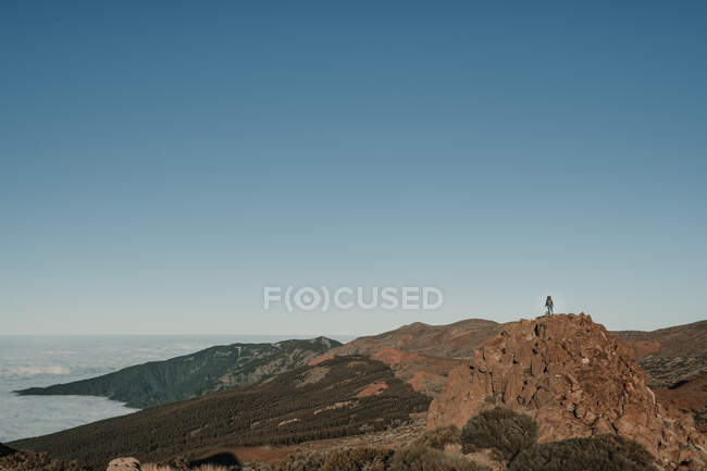 Turista irreconocible de pie en la cima de la colina lejos en un día sin nubes - foto de stock