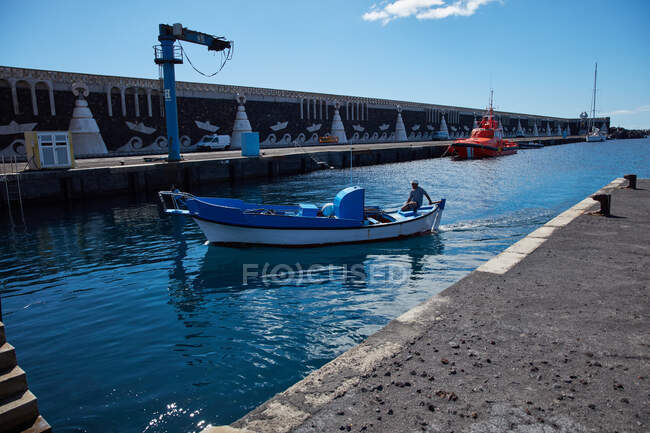 Lungomare della città con acqua blu nella baia e barca a motore a vela alla luce del sole, El Hierro — Foto stock